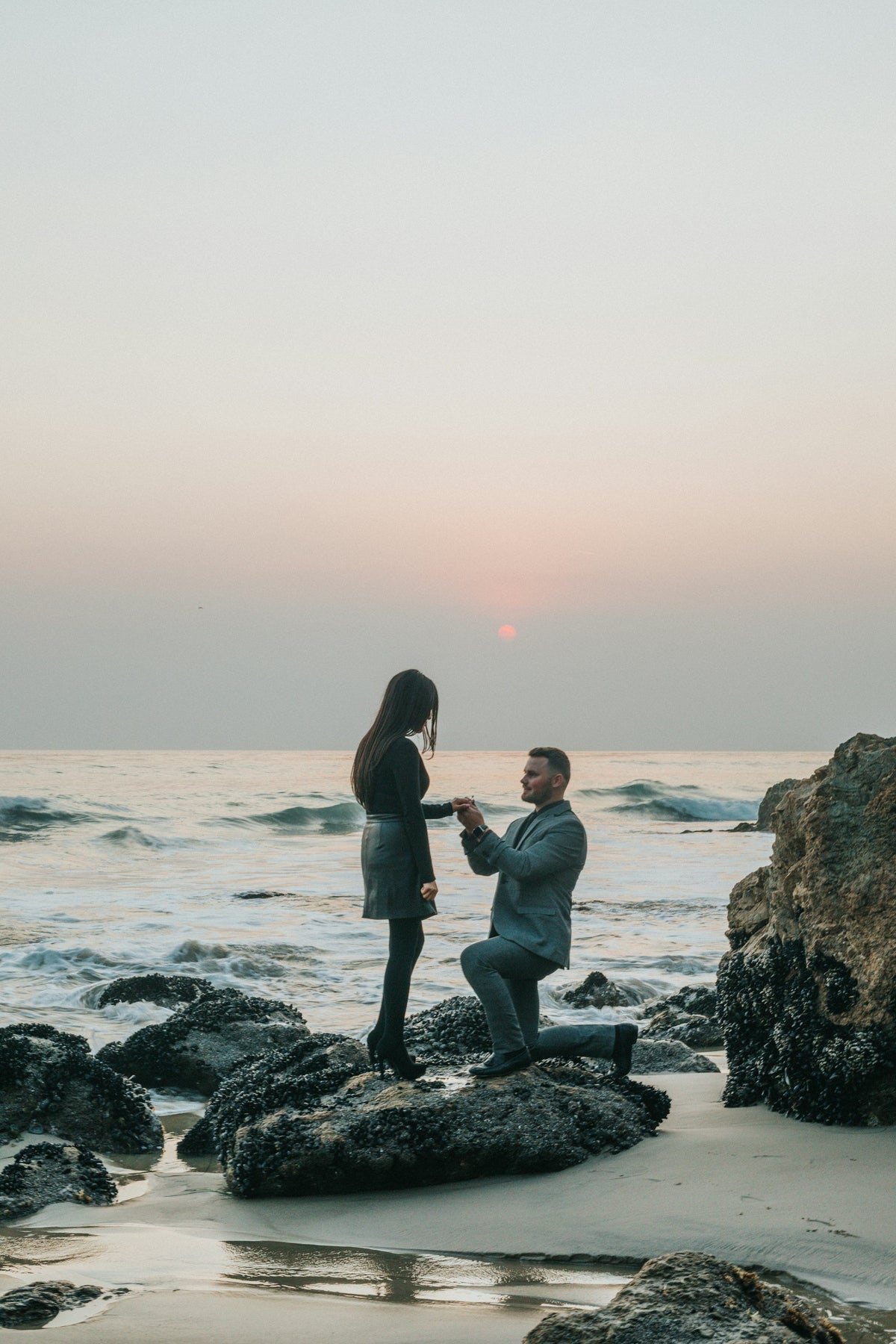 Man proposing on one knee on rocks by the sea